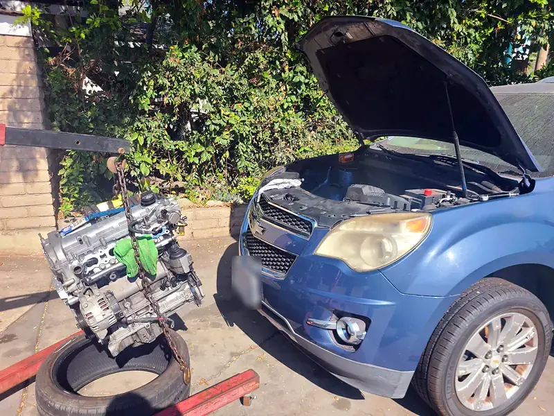 The engine out of a Chevy Equinox, hanging from the shop crane beside the car