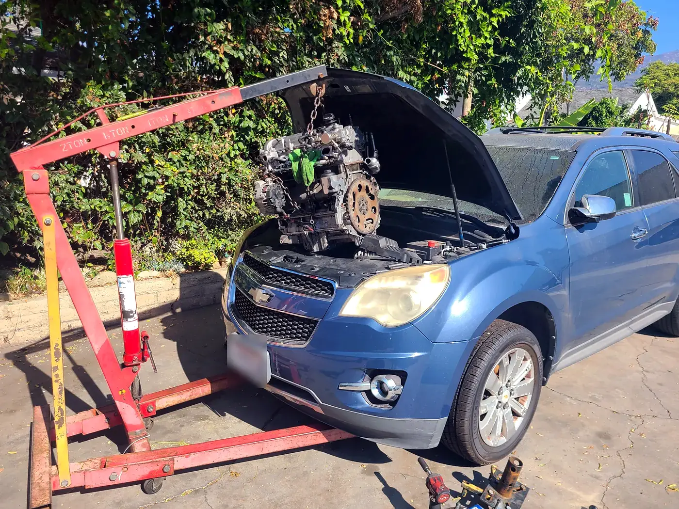A Chevy Equinox with its engine lifted out on a shop crane in the yard at Beach Motor & Tires