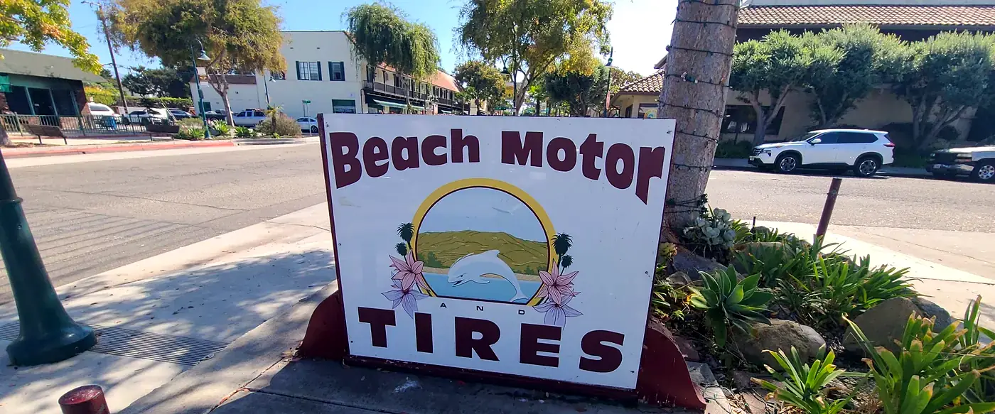 The Beach Motor & Tires sign on Carpinteria Ave, a dolphin over the beach and hills, with downtown Carpinteria behind it